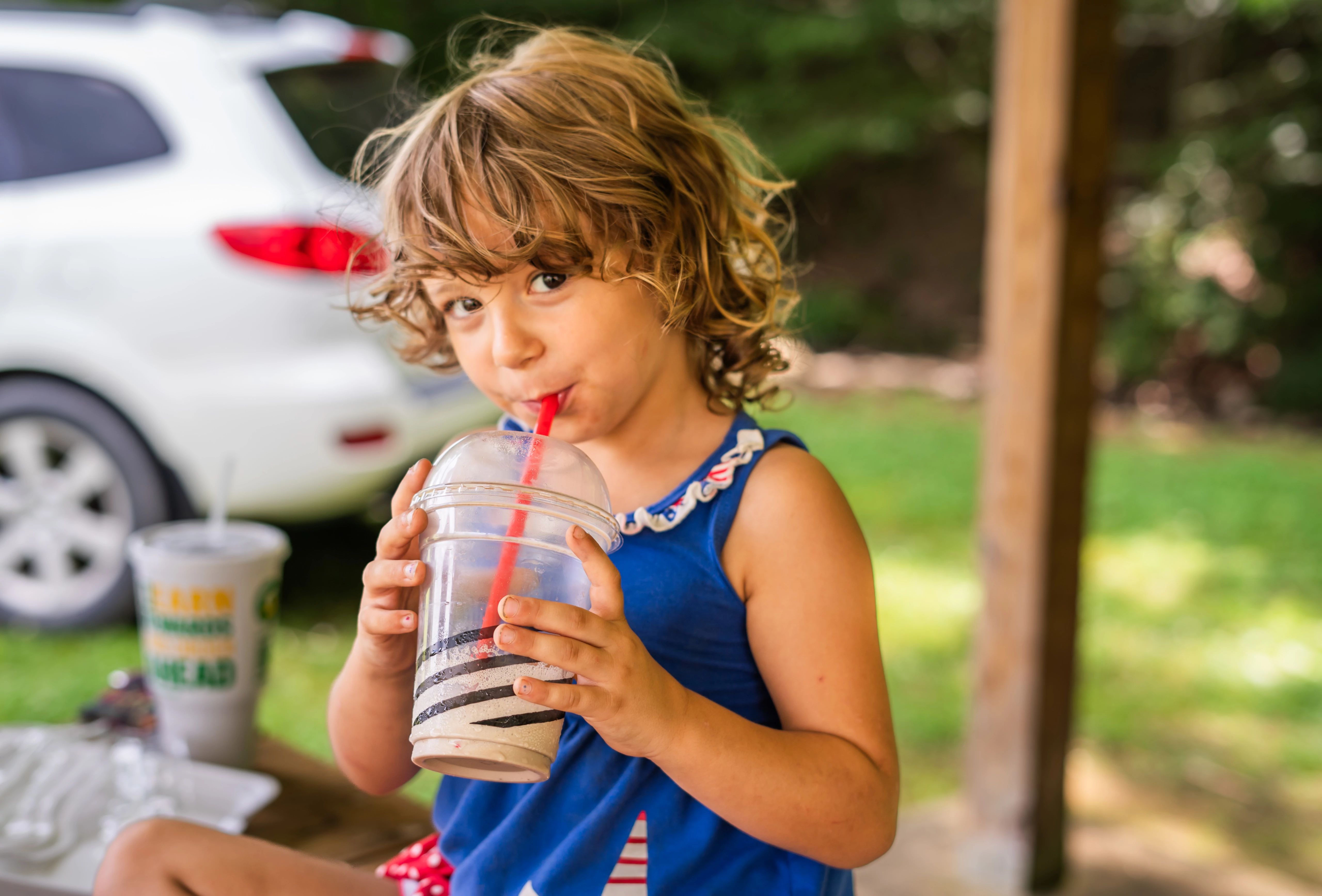 a young child drinks from a large cup while at a park