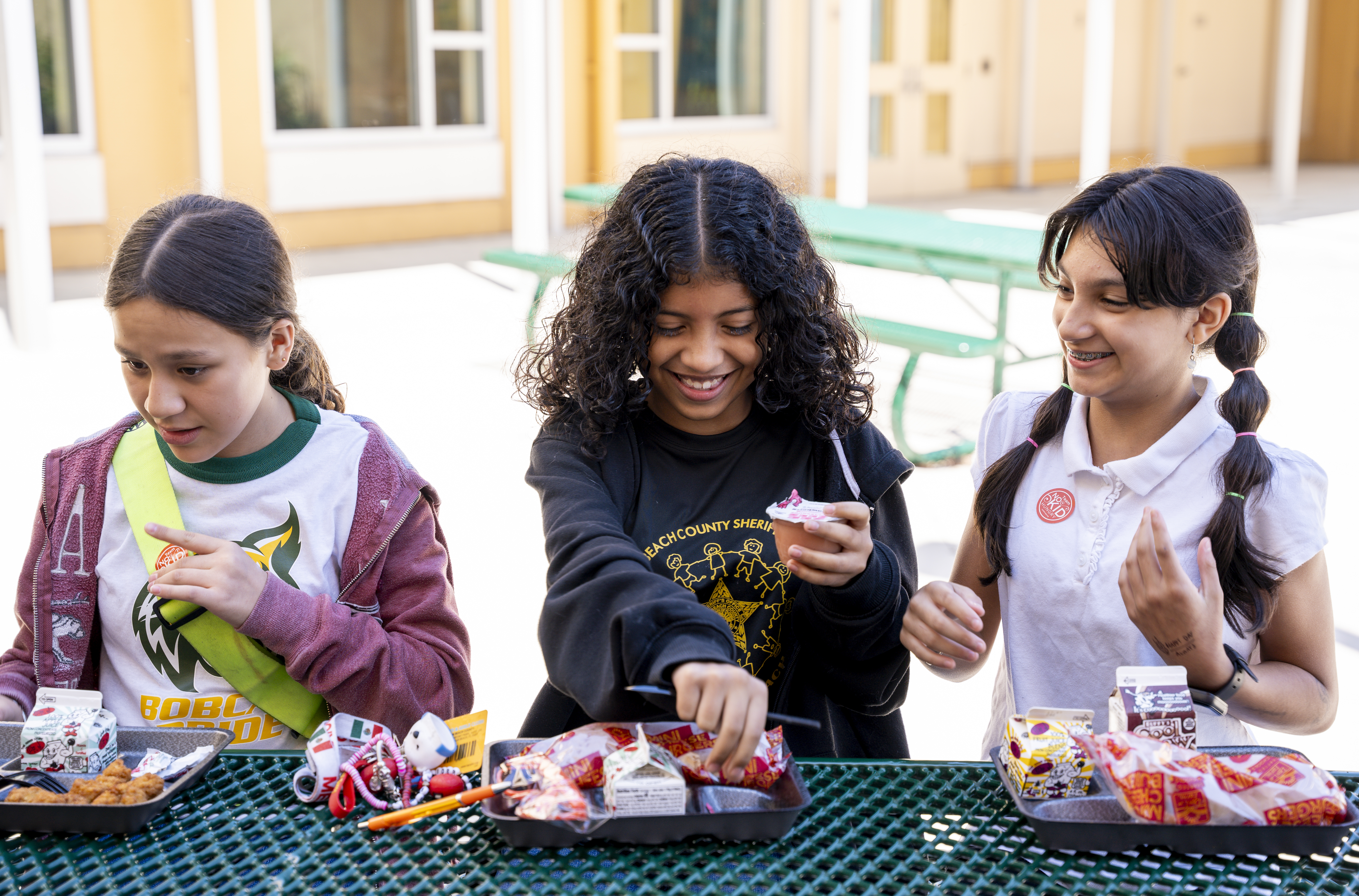 three girls sit outside and eat breakfast. 