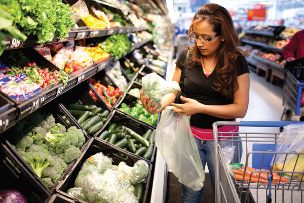 A woman bags up broccoli in a grocery store produce aisle
