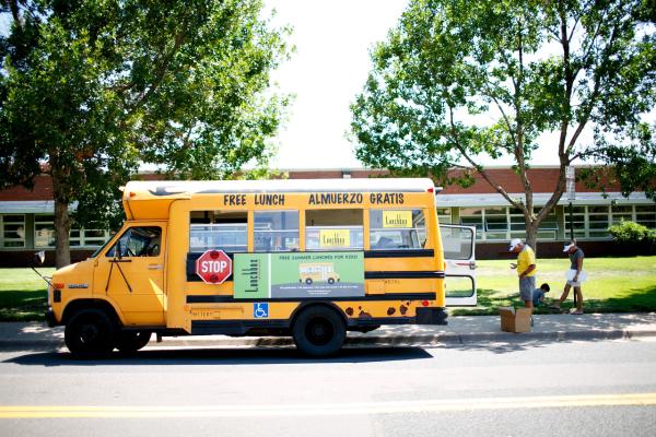 school bus offering summer meals is parked outside a school building. 
