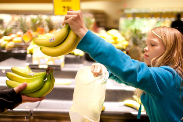 girl selecting bananas in a grocery store. hero image size
