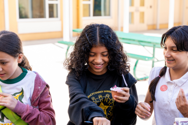 three young girls eat breakfast outside and laugh