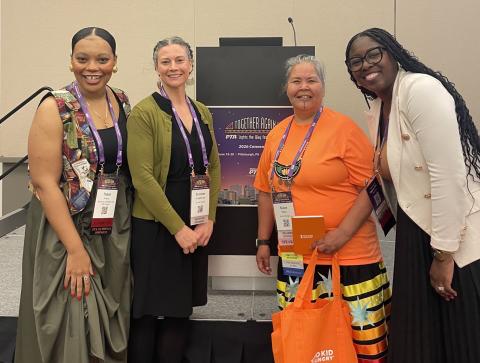 Topaz, Chioma, Bewaush, and Summer taking a picture in front of a podium at the PTA conference